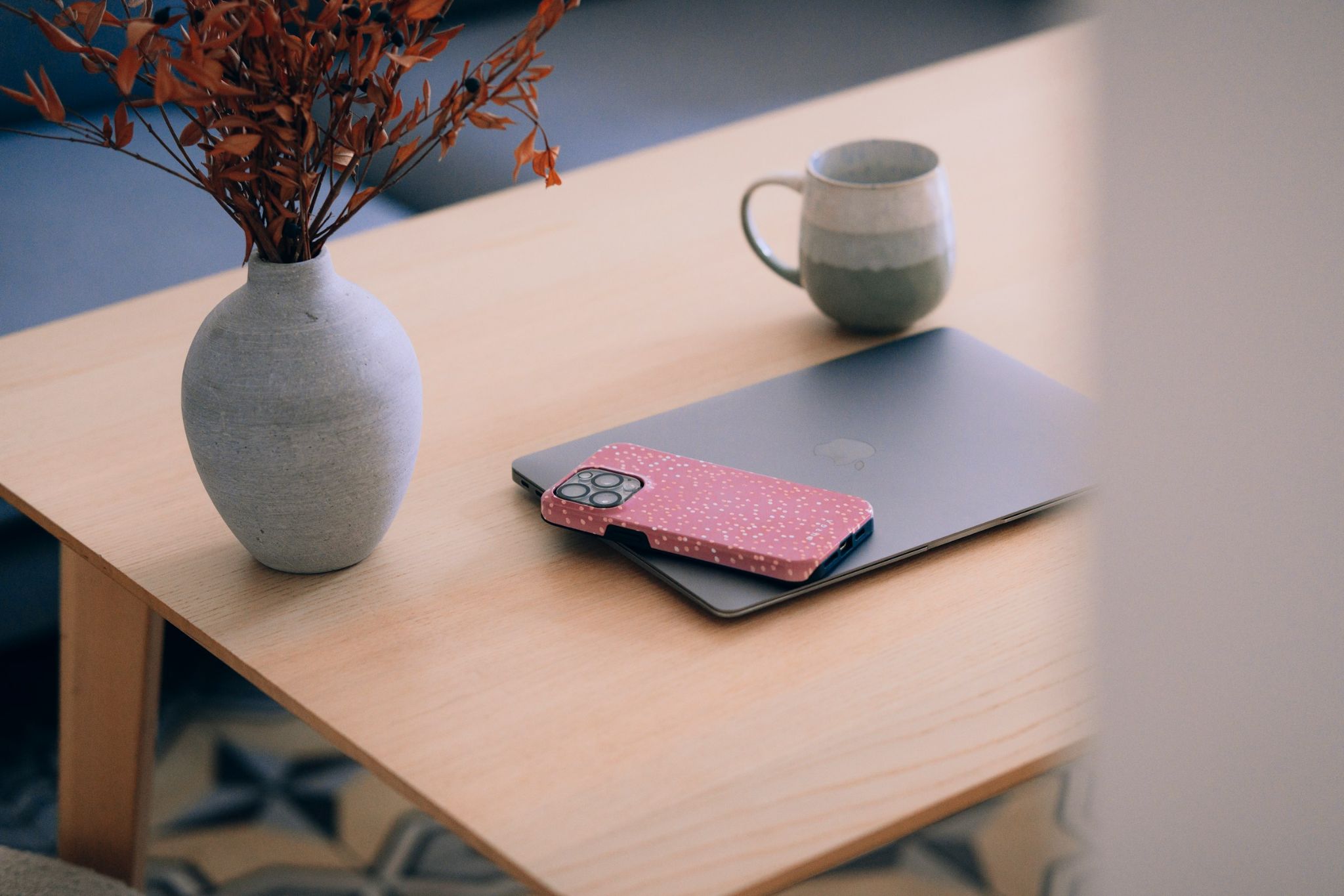 A laptop, phone, and coffee mug sitting on a wooden table — the always-on work phone that never turns off.